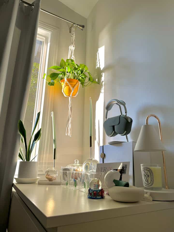 A white bedroom corner bathed in soft morning light featuring plants and candles creating a peaceful atmosphere