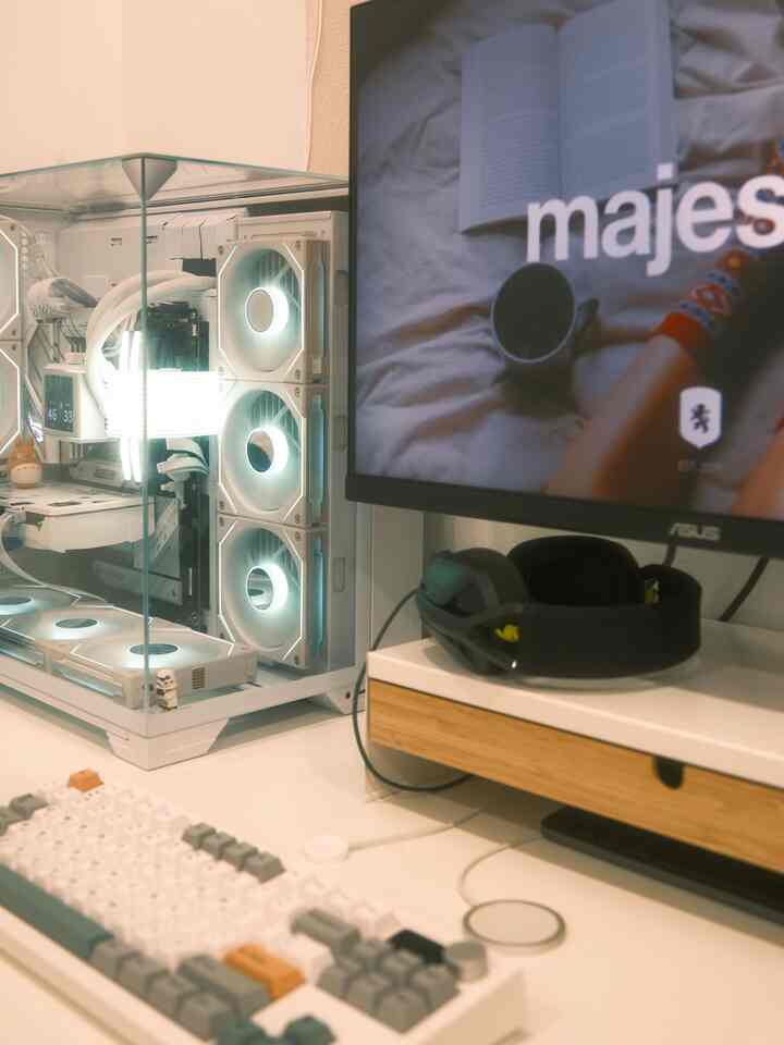 A clean white and wood-toned home office featuring a gaming desk with monitor and RGB-lit PC setup