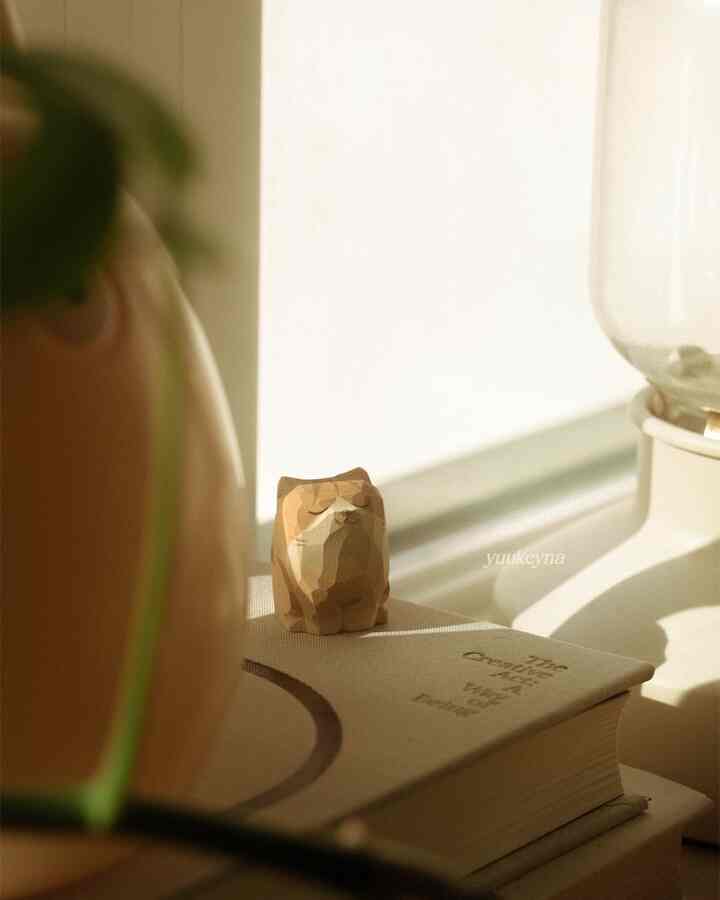 Cozy interior featuring a wooden cat figurine and books on a desk in warm natural tones