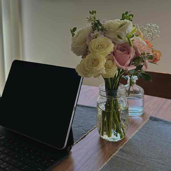 A cozy kitchen dining table in natural and wood tones featuring vases with flowers and an iPad