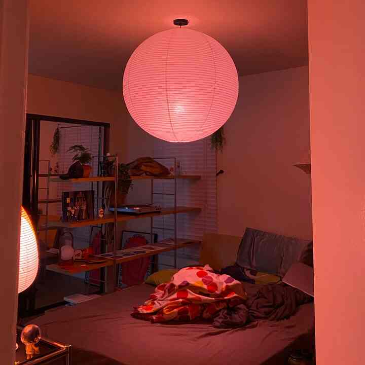 Cozy compact bedroom bathed in warm orange light featuring natural wood-tone shelves and a messy bed