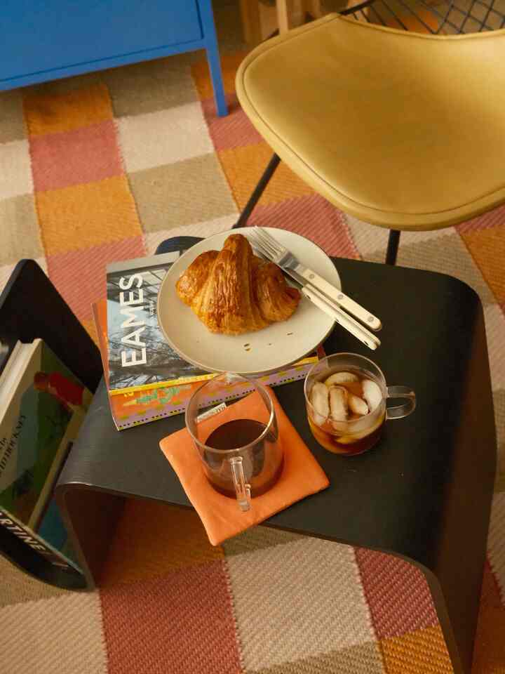 Warm orange and beige toned living room featuring a black coffee table with a plate of croissant and two coffee cups in a cozy home cafe style