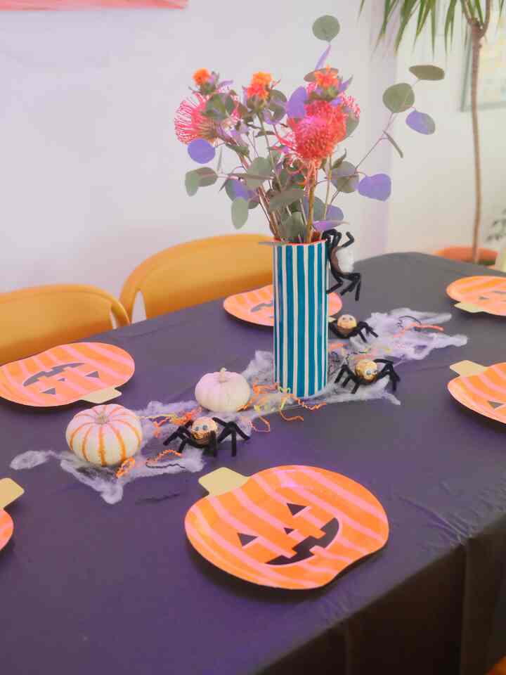 A cozy dining room with a black tablecloth and mustard dining chairs, decorated with Halloween props and a vase of flowers