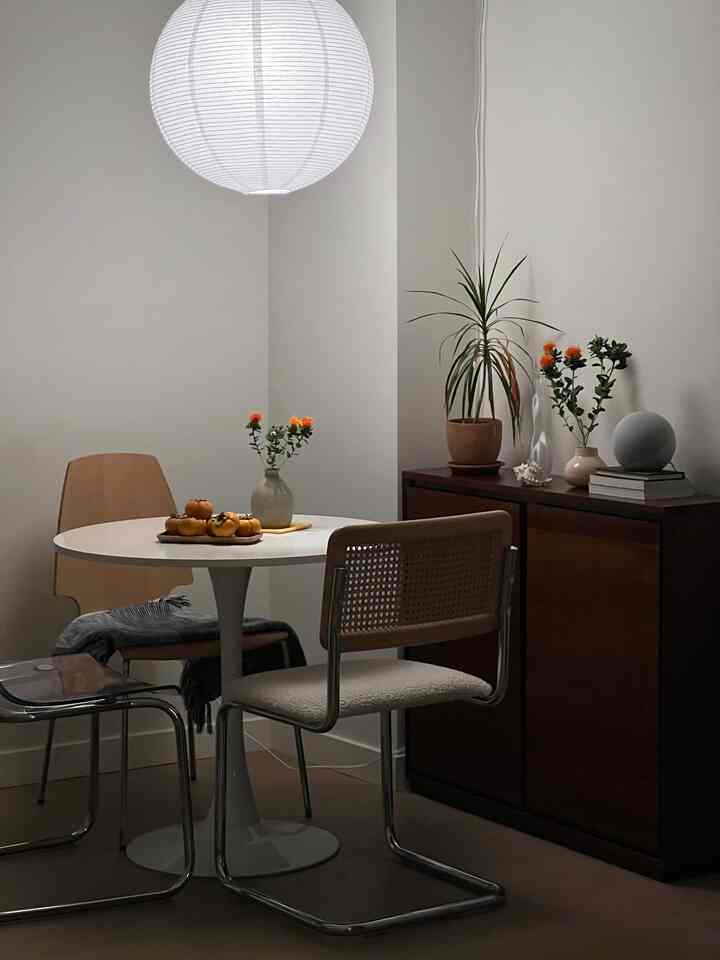 Minimal dining room in white and brown tones, featuring a round dining table, rattan chairs, and warm pendant lighting for a cozy feel