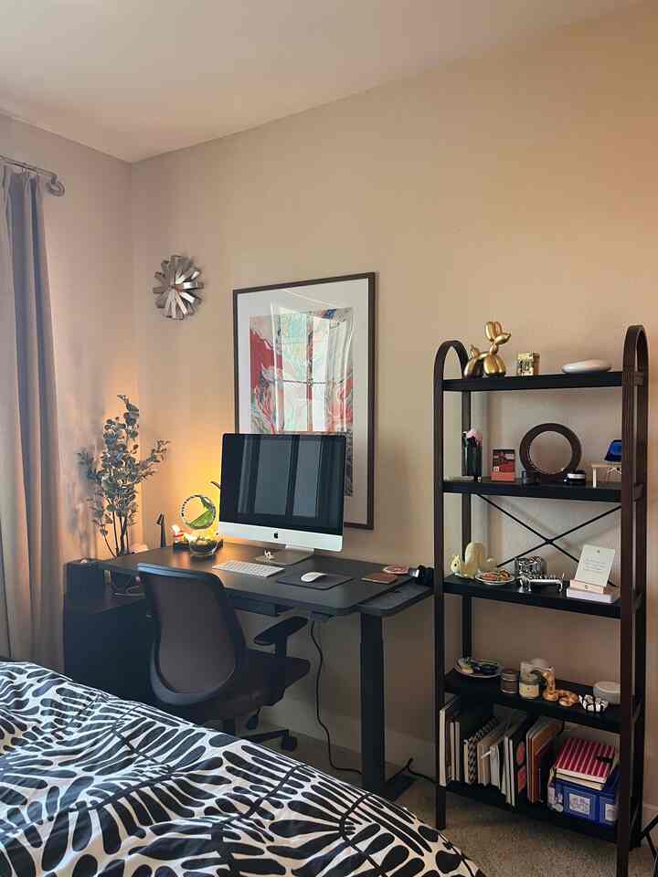 Beige-walled, modern small bedroom featuring a standing desk, office chair, and organized bookshelf with cozy atmosphere