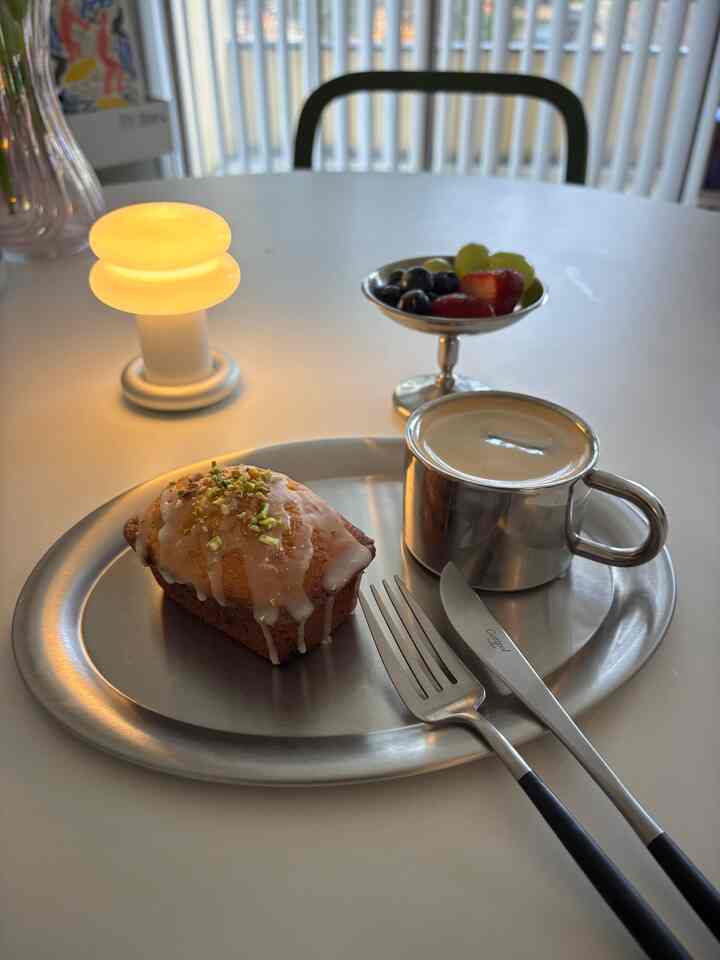 Cozy home cafe setting on a silver dining table featuring a lemon cake, coffee in silver cup, and a small fruit dish on a round table