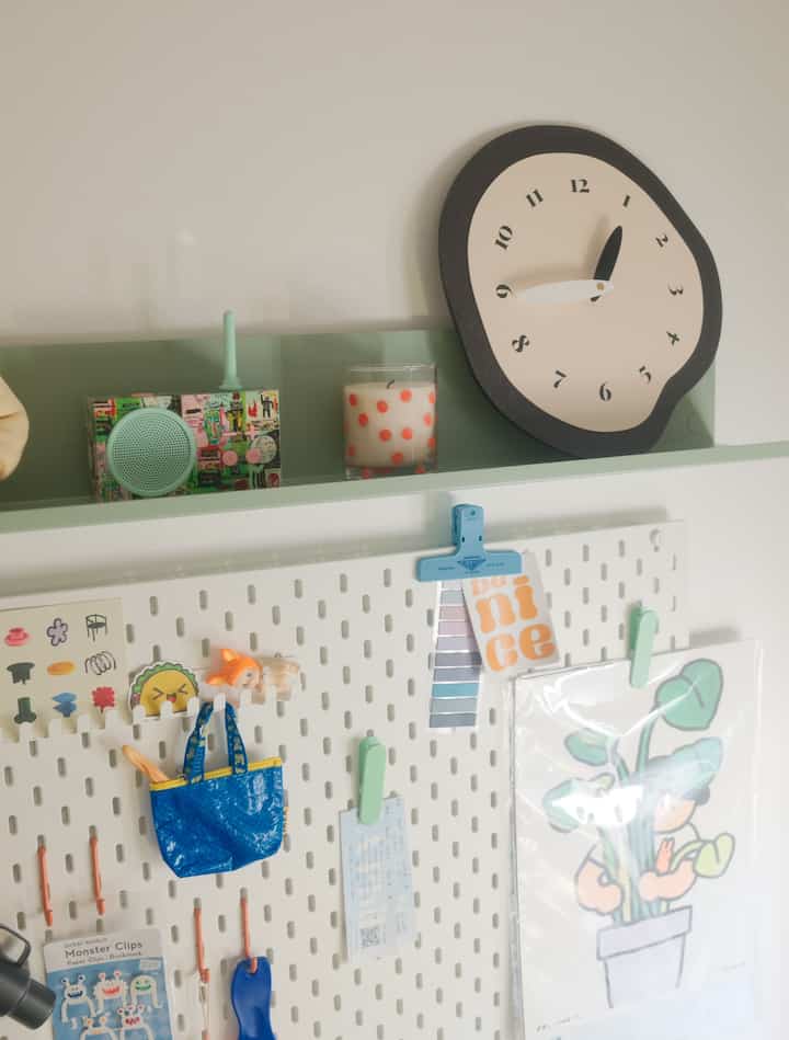 Minimal interior space with white walls and green shelf, featuring an irregular shaped silent wall clock and a small vintage radio on the wall
