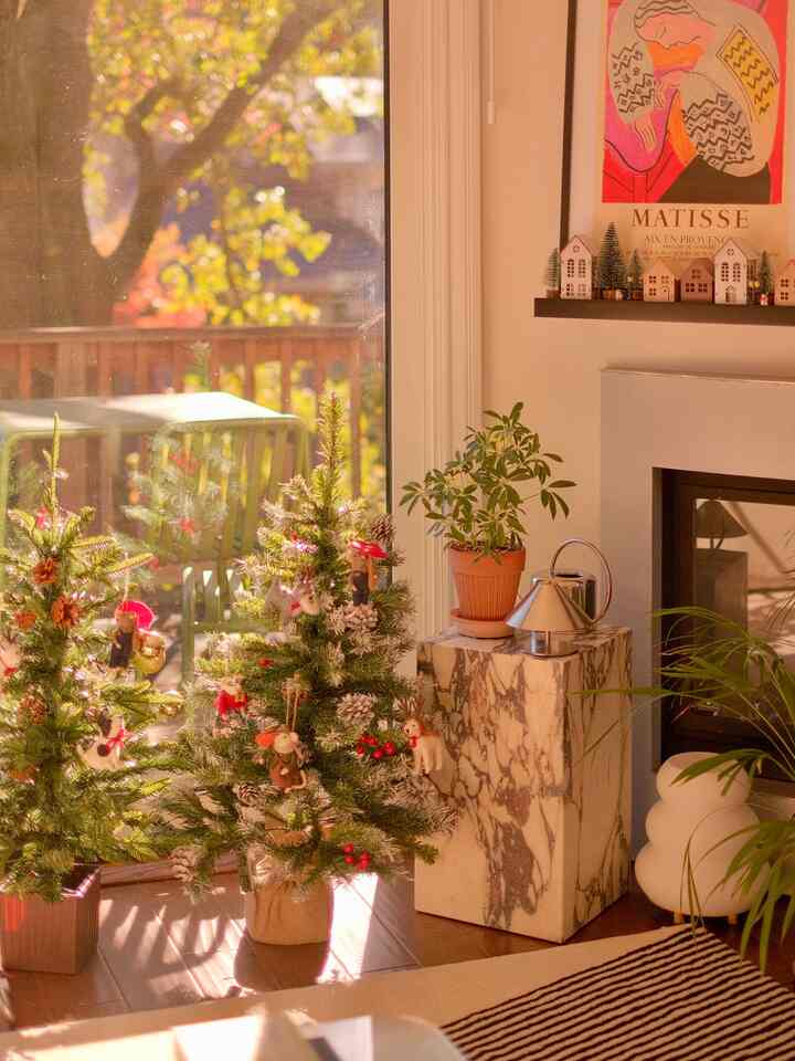 Cozy living room corner in white and brown tones featuring decorated Christmas trees and a marble plinth