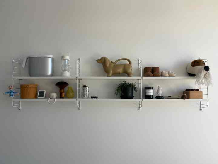 White-toned nursery wall with shelves displaying dog-shaped objects and baby shoes, creating a natural and organized space
