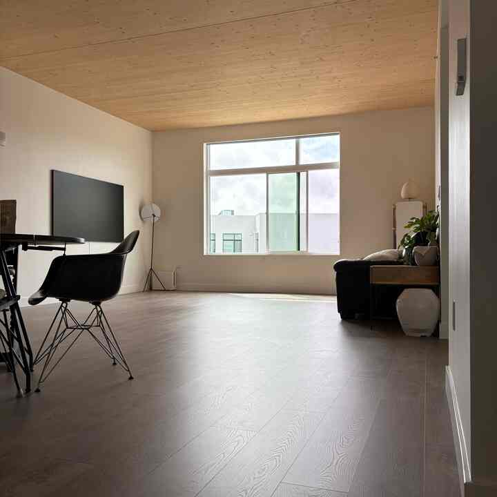 Natural color-toned minimalist living room featuring wood tone ceiling, black sofa, and mid-century modern armchair