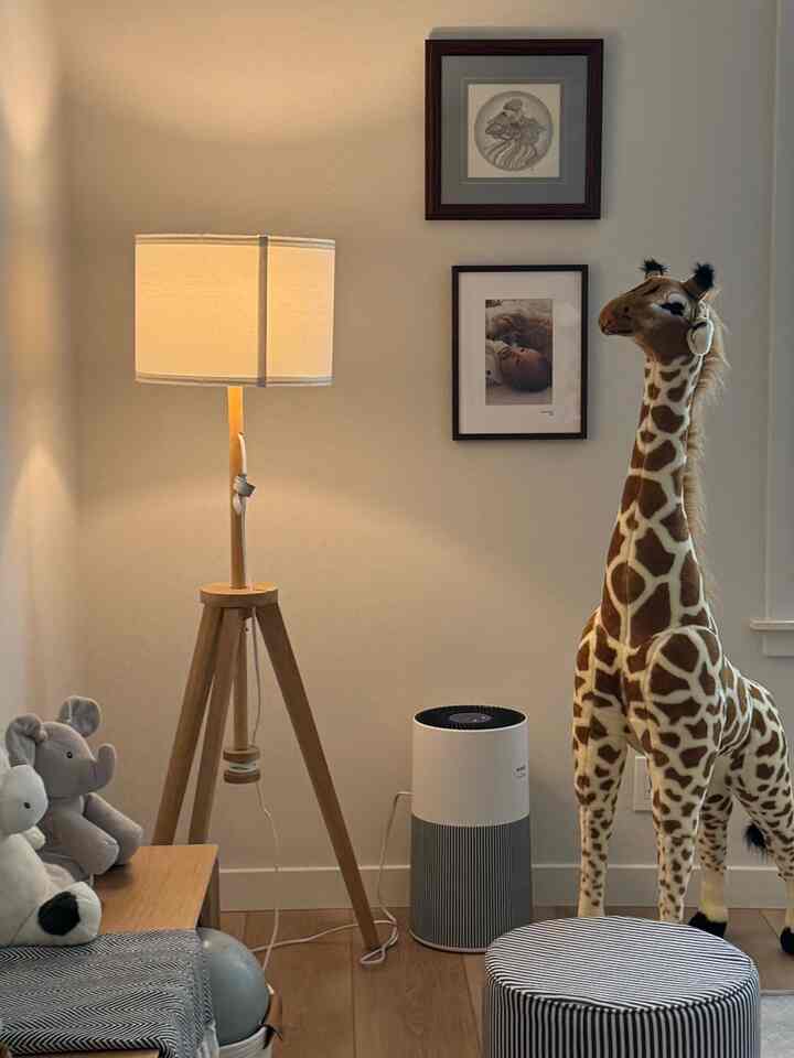 Warm beige kids' room featuring a wooden floor lamp, large giraffe plush, and striped ottoman creating a cozy atmosphere