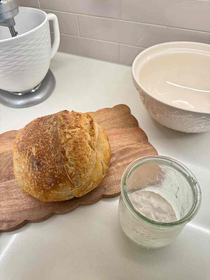 A white and natural wood tone kitchen countertop featuring a Mason Cash bowl and freshly baked sourdough bread with baking tools