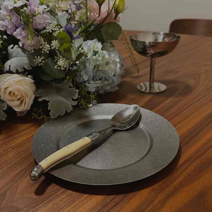 A brown wood tone dining table featuring silver cutlery and a vase with flowers, creating a refined dining atmosphere