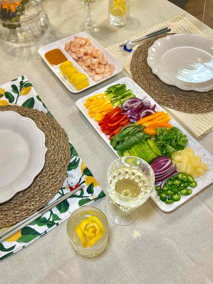 Beige linen tablecloth and natural round woven placemats on dining table with shrimp, fresh veggies, and wine glasses in a cozy dining setting