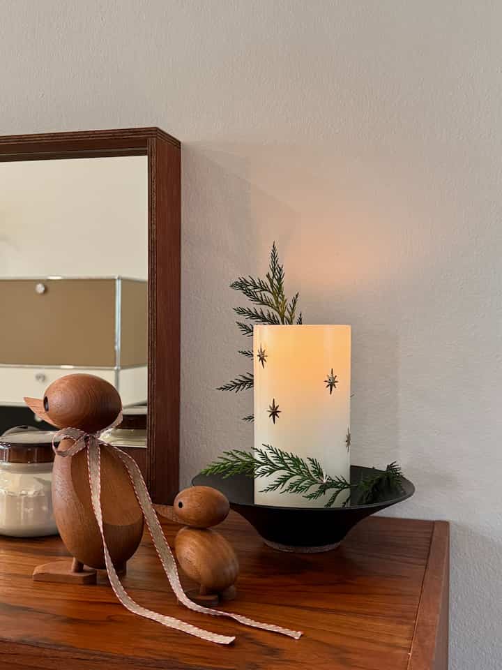 Cozy space with white walls and wood tone table featuring a lit candle and wooden duck decorations