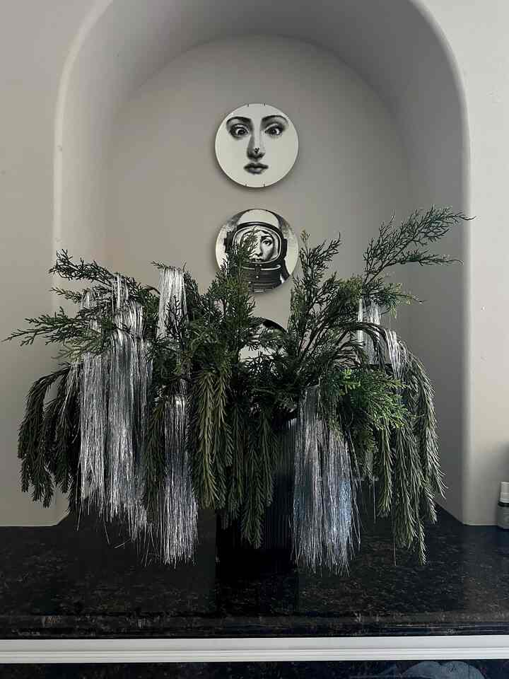 Stylish interior decoration with green artificial cedar stems and silver tinsel in a vase, beneath an arched wall niche holding face-patterned plates