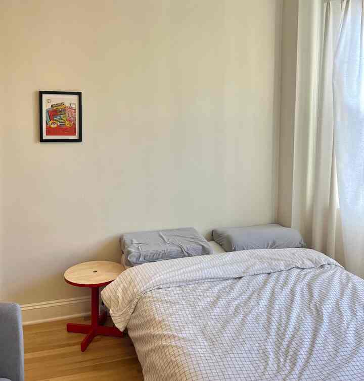 White and wood tone bedroom featuring red side table and neat duvet cover with a cozy peaceful atmosphere