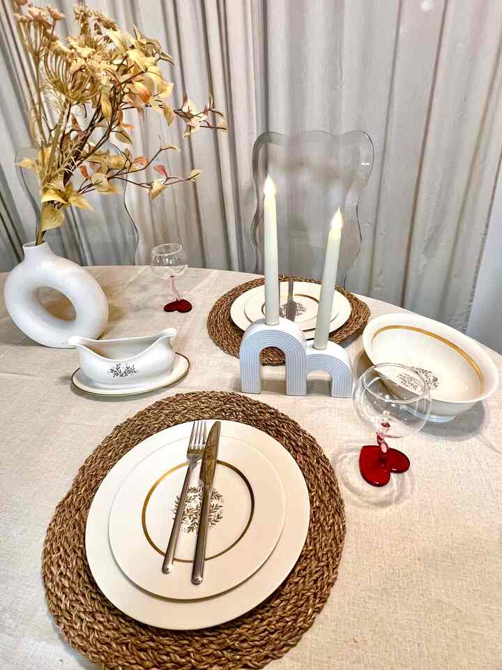 Beige and white toned dining room featuring dried floral vase, candles, and wine glasses arranged on linen tablecloth for cozy home party ambiance
