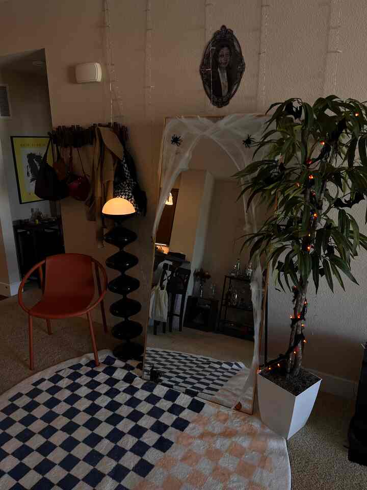 Beige and brown toned living room featuring a large full-length mirror decorated for Halloween, green plant, and a checkerboard rug in a simple interior