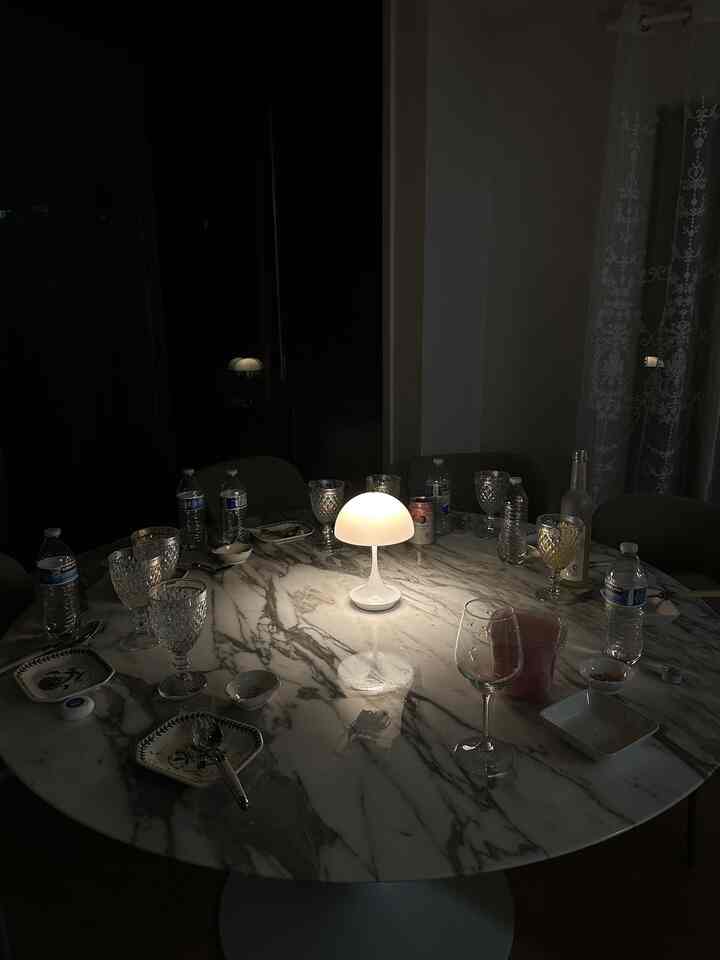 Dark-lit dining room featuring a white round marble table with a bright table lamp at the center
