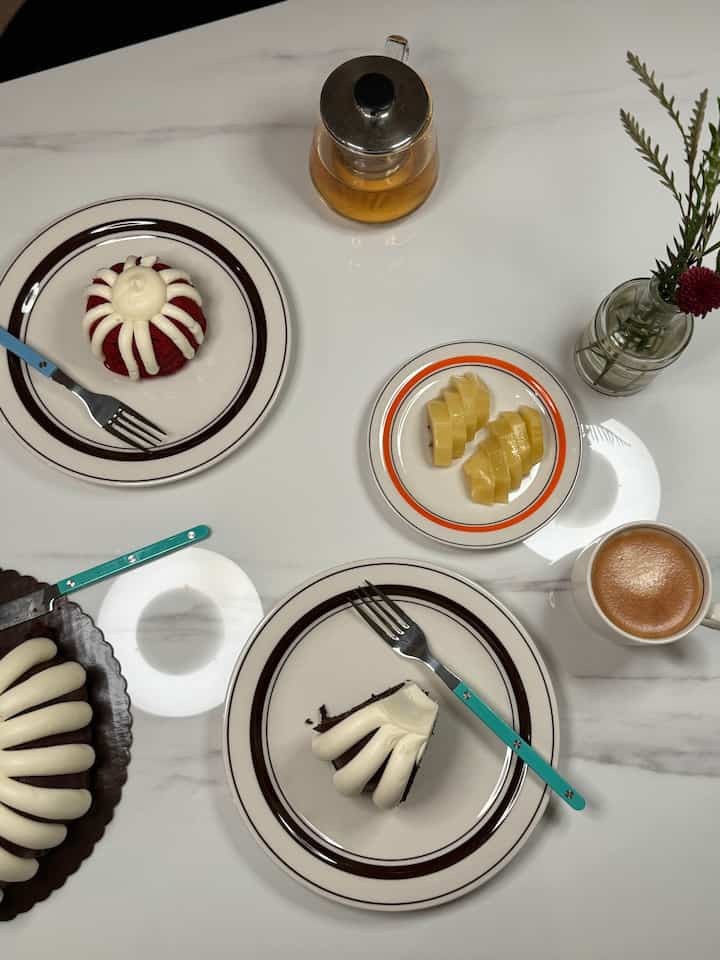 White tone dining table featuring cakes, coffee, and a flower vase in a cozy home cafe setting