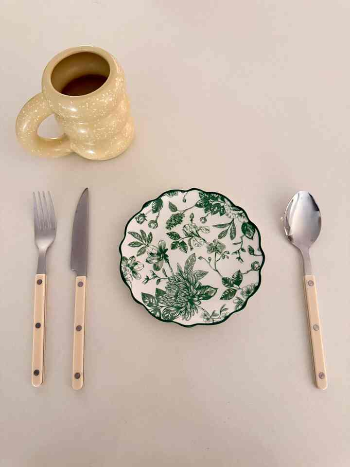 A beige and white toned table featuring a floral plate, silver cutlery, and a beige mug arranged in a cozy table setting