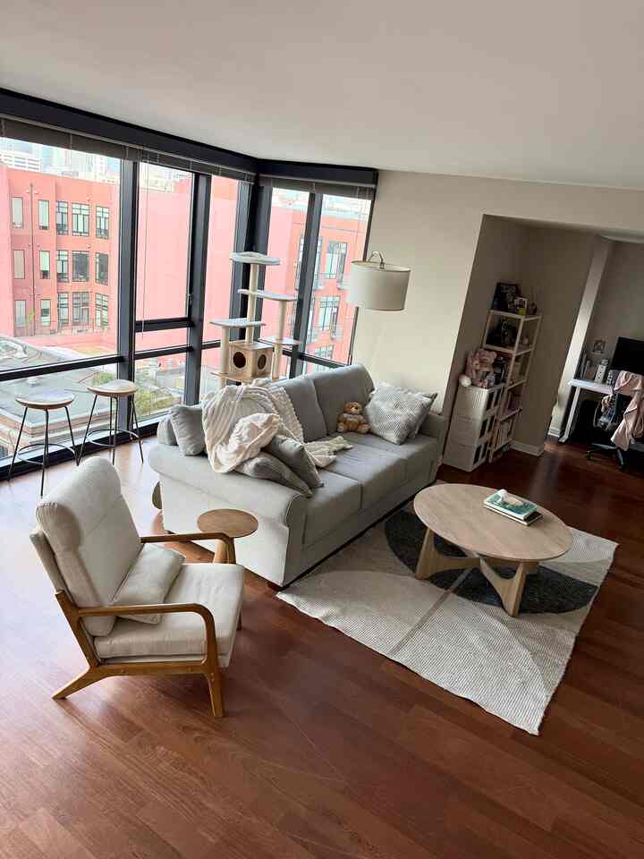 Cozy living room with warm wood floors, natural fabric sofa and armchair, featuring cat tower near large windows