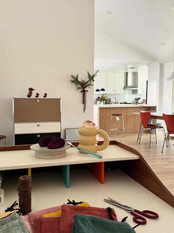 White and brown toned kitchen and dining room featuring a yellow bold mug, purple plums, and red chairs in a cozy kitchen space