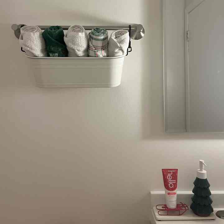 White-walled bathroom featuring a metal towel rack with neatly rolled white and green towels, creating a cozy atmosphere