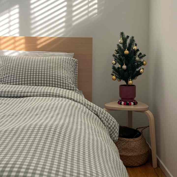 Natural tone bedroom featuring checkered bedding and a wooden stool with a small Christmas tree, creating a cozy atmosphere