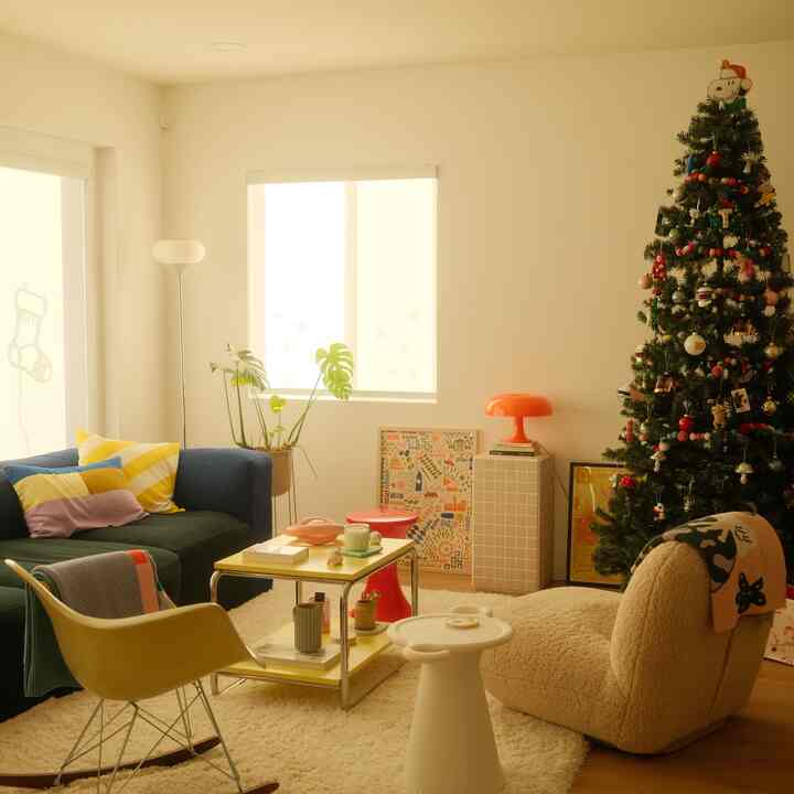 Warm beige, navy, and yellow-toned living room featuring a decorated Christmas tree, cozy sofa, and armchair under soft golden light