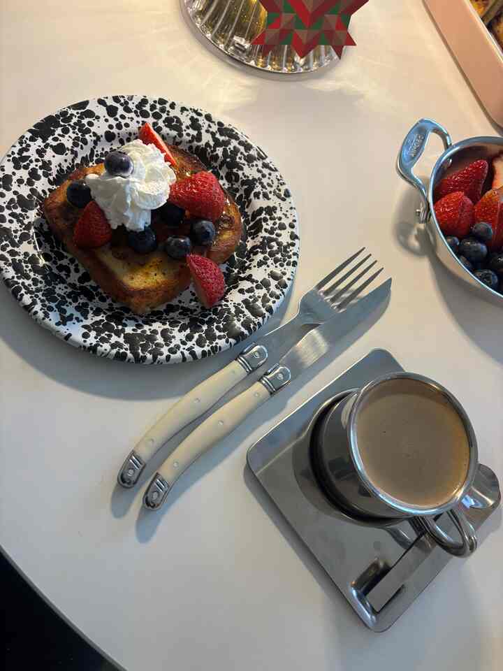 A simple home cafe brunch setting on a white table featuring black and white plate, cutlery, and stainless steel coffee cup