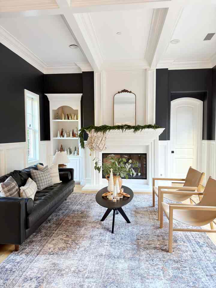 Black and white toned living room featuring black leather sofa, natural leather armchairs, fireplace, and Christmas garland in a warm atmosphere