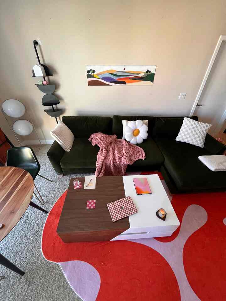 Living room with beige walls and a vivid orange and lavender rug, featuring an olive green sofa and wooden table creating a cozy atmosphere