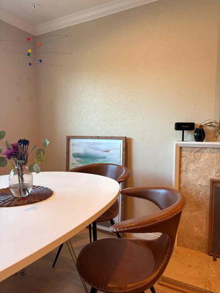 Warm beige-walled dining room featuring brown leather chairs and a white dining table with a vase and colorful mobile, creating a cozy atmosphere