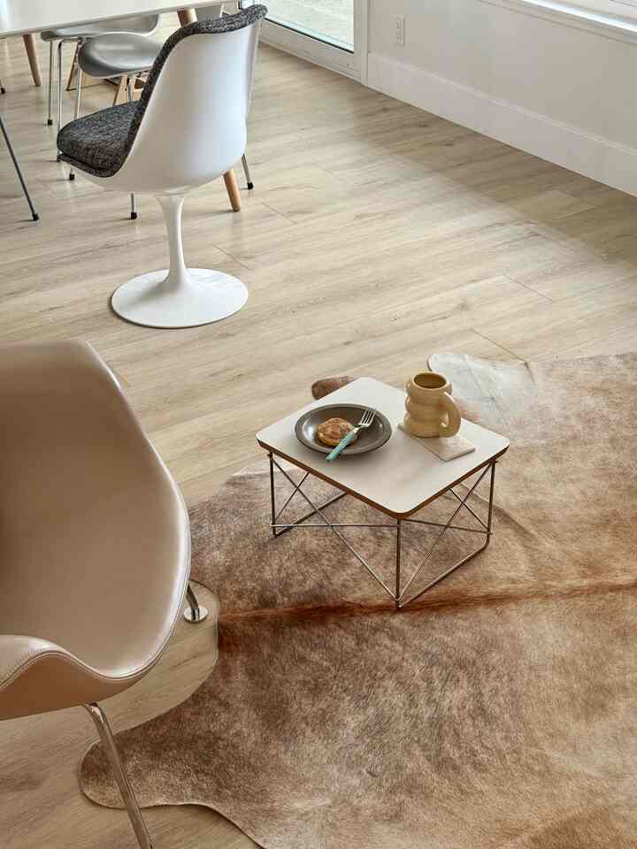Natural wood-tone flooring with modern, simple armchairs and a coffee table positioned in a partial dining room space