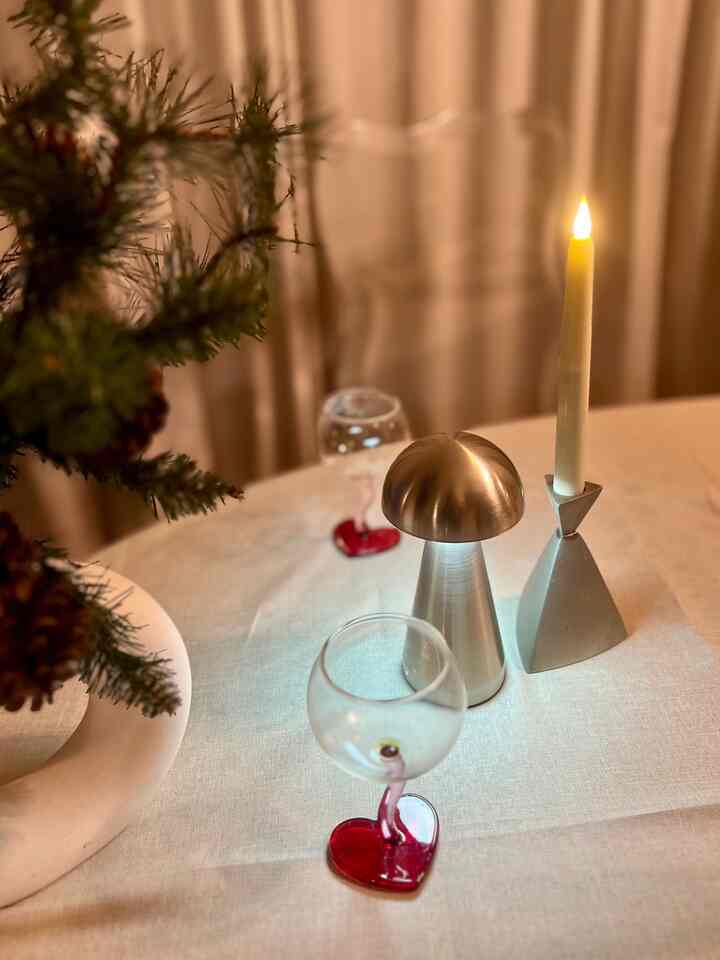 Warm beige-toned table setting featuring heart-shaped wine glasses, a chrome silver mushroom table lamp, and a lit candle