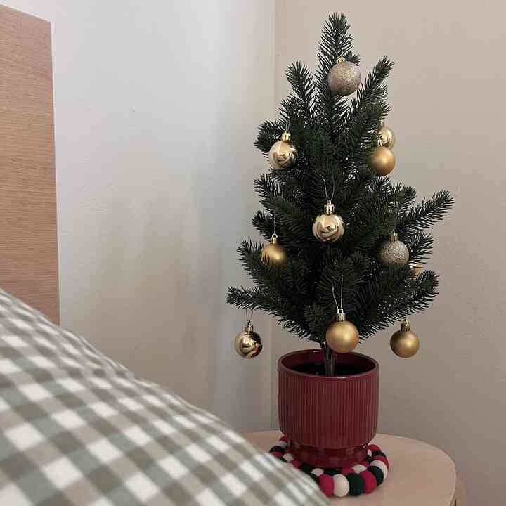 Bedroom with white walls and wood-tone table featuring a green mini Christmas tree decorated with gold ornaments