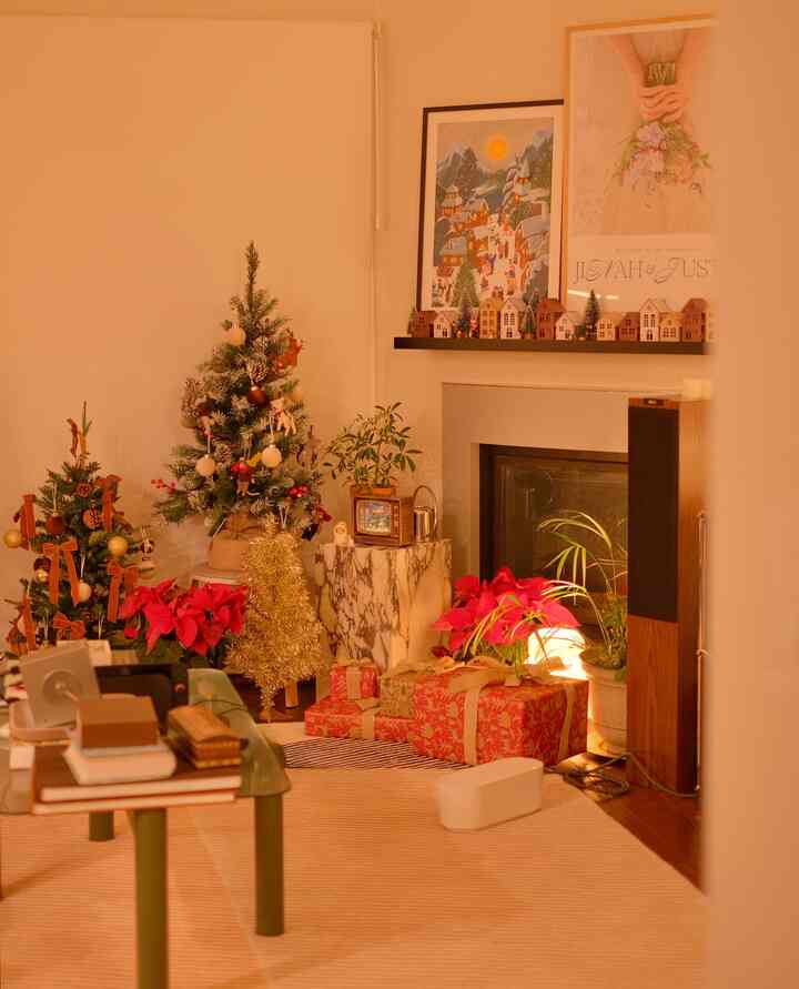 Beige-toned living room corner featuring decorated Christmas trees, red poinsettias, gold tree, and wrapped gifts creating a warm festive atmosphere