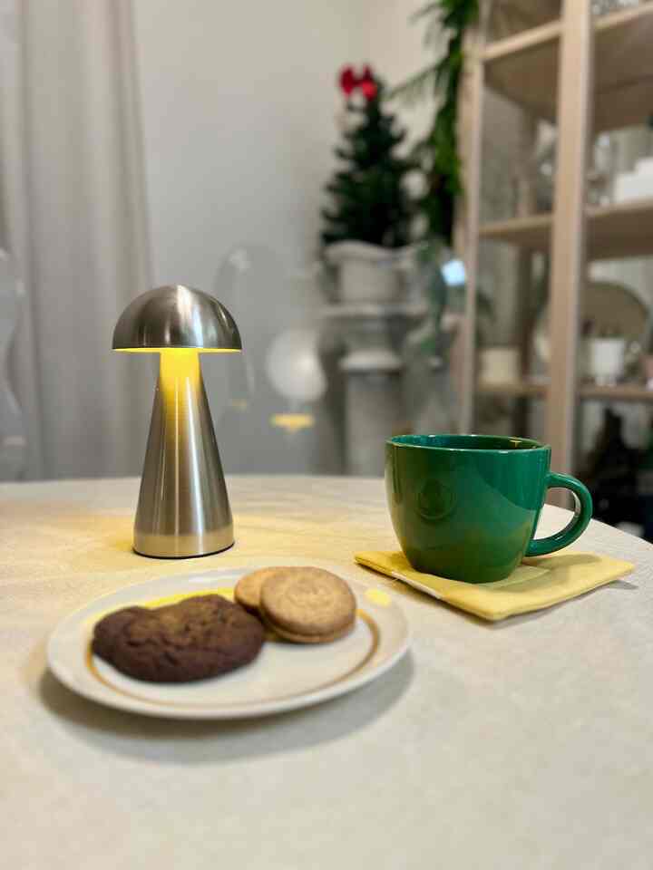 Warm beige toned home cafe table featuring a silver mushroom table lamp, green cup, and cookies creating a cozy atmosphere