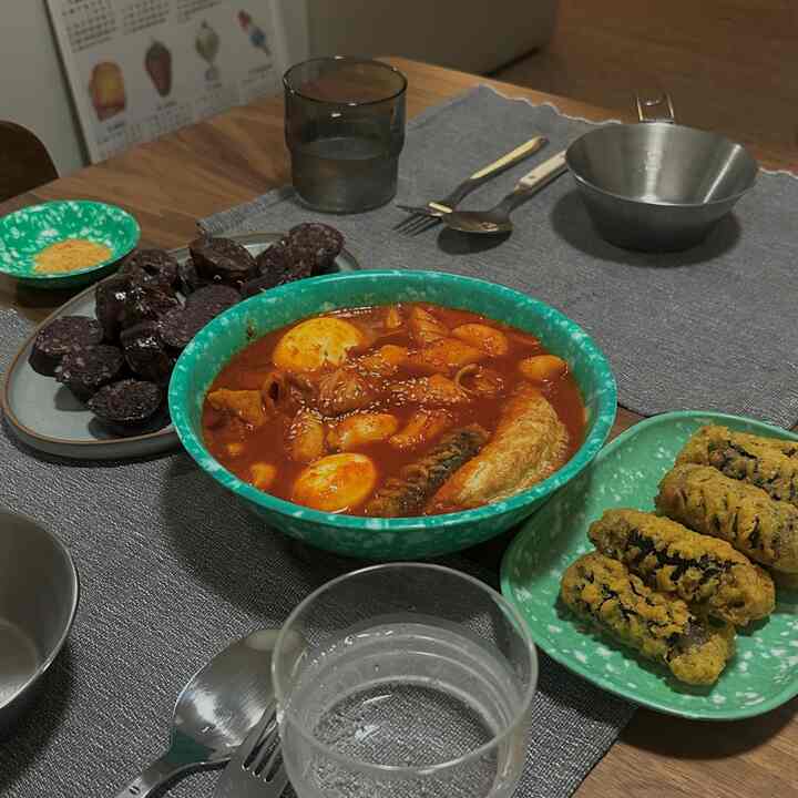 Dining room table with gray placemat and green bowls featuring various Korean street foods