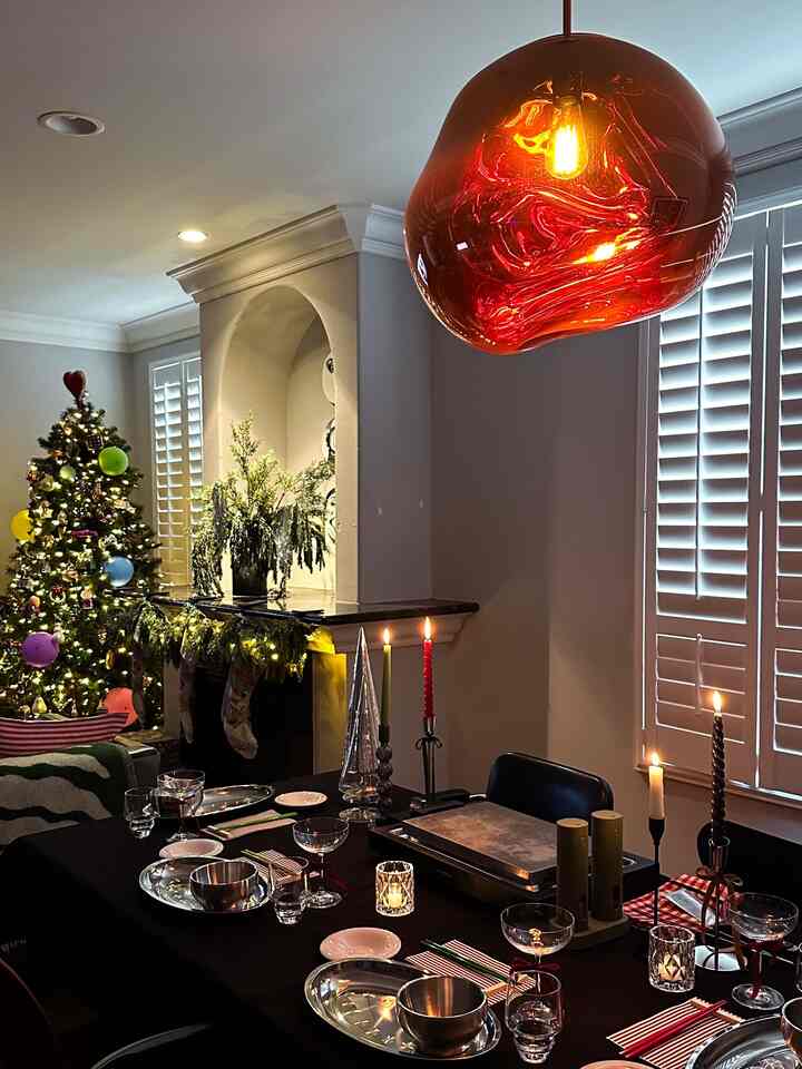 Warmly lit dining room featuring a black tablecloth-covered dining table with a teppanyaki grill, decorated Christmas tree, and candles for a festive home party atmosphere