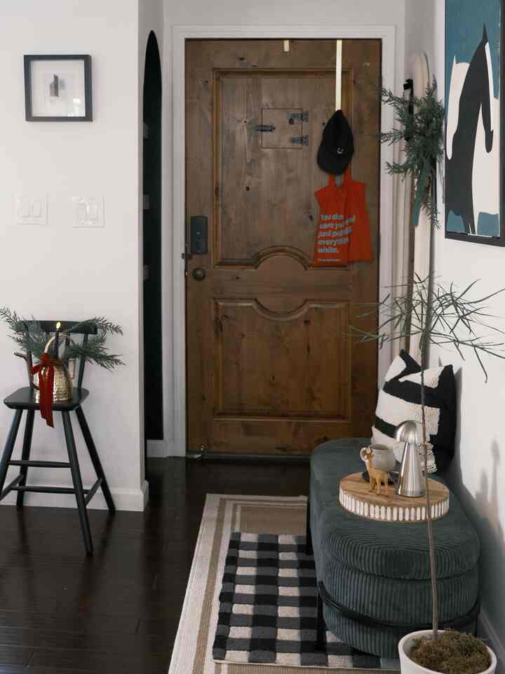 A wood tone and black entrance space featuring a modern stool and cushion with a natural vibe