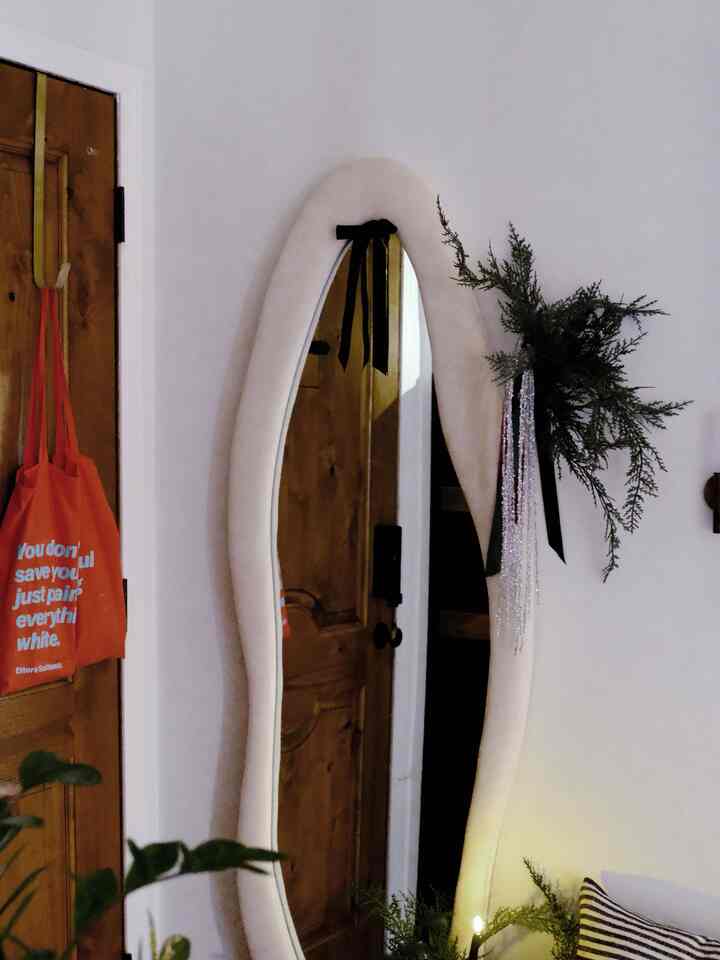 Natural color walls and wooden door in an entrance space featuring a large organically shaped mirror and plants, creating a cozy atmosphere