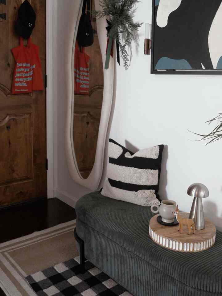 Bright white walled entrance featuring dark gray sofa with black striped cushion and classic wooden door