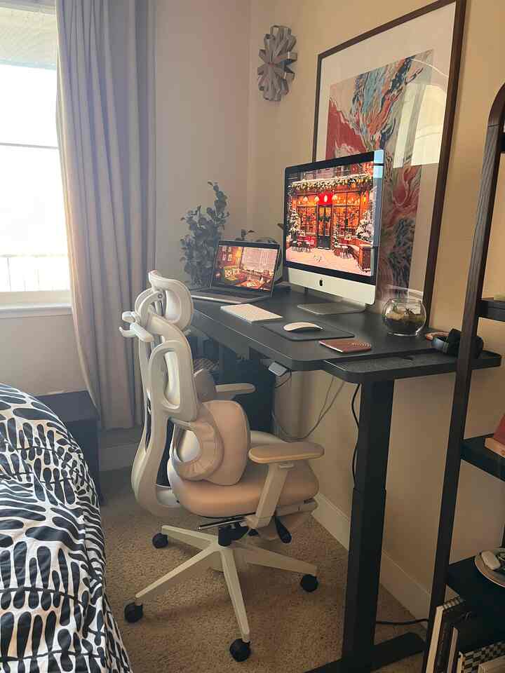 Beige walls and carpet frame a compact home office featuring a white standing desk and ergonomic chair in a tidy workspace