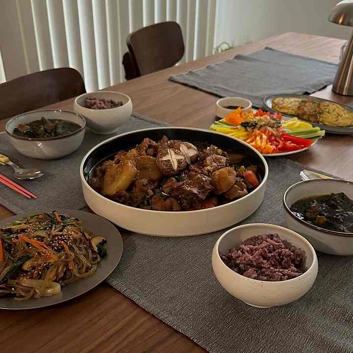 Brown wood-tone dining room with a central table and chairs, featuring various Korean dishes and bowls creating a warm atmosphere