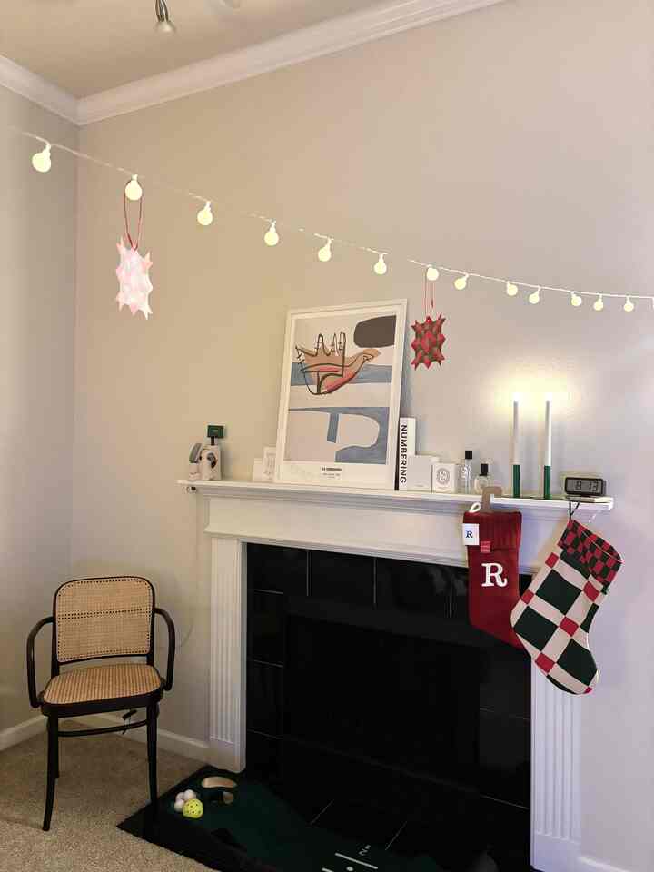 White-walled living room with fireplace, decorated with Christmas garland lights and armchair in a cozy setting