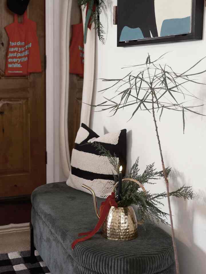 A cozy entrance corner featuring a green ottoman with golden accents, black candlelight, and greenery decorations