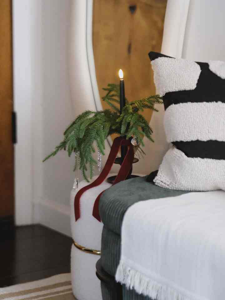 Black and white accented living room corner featuring green sofa, textured cushions, lit candle with natural greenery creating cozy ambiance